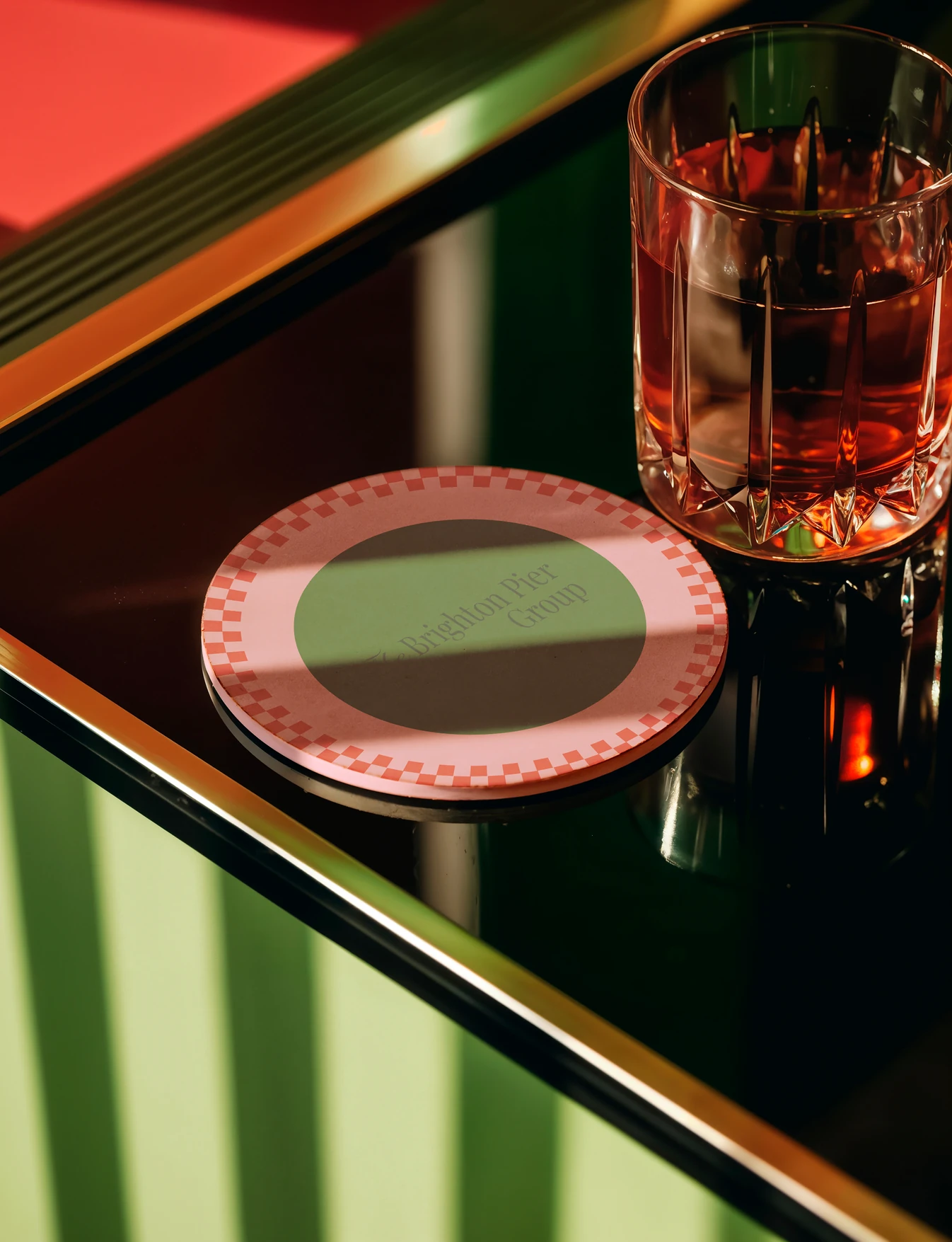 A branded coaster and a tumbler on a green glass table