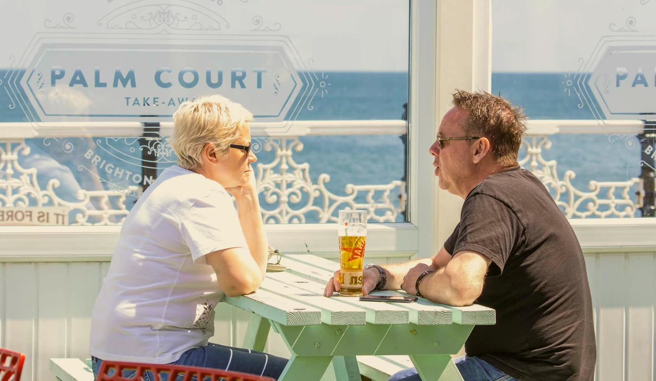 Two people at a table in Palm Court, the sea behind them