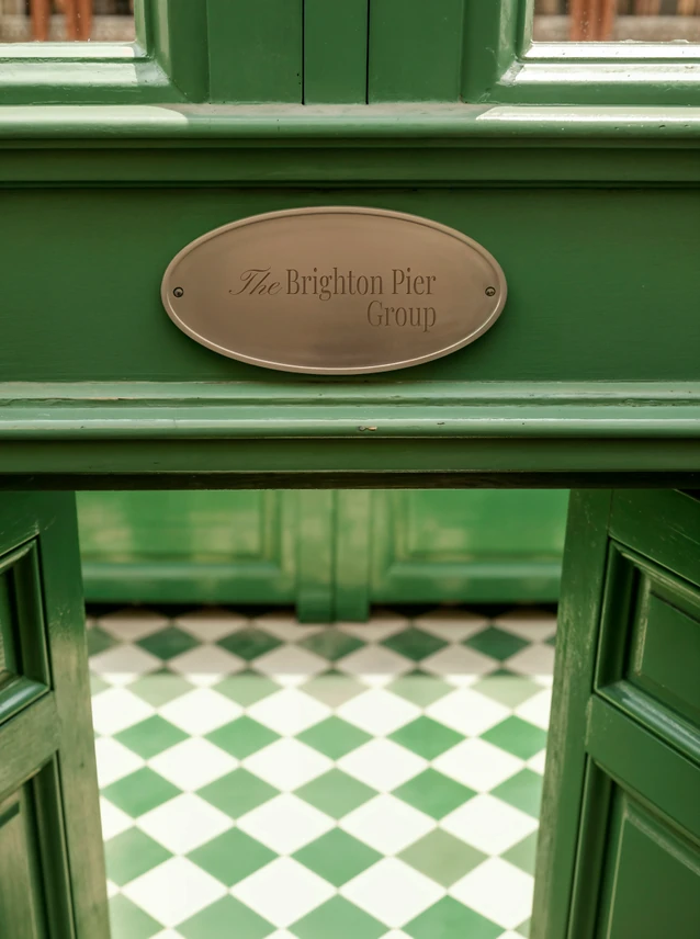 A brass wordmark plaque on a green painted shopfront