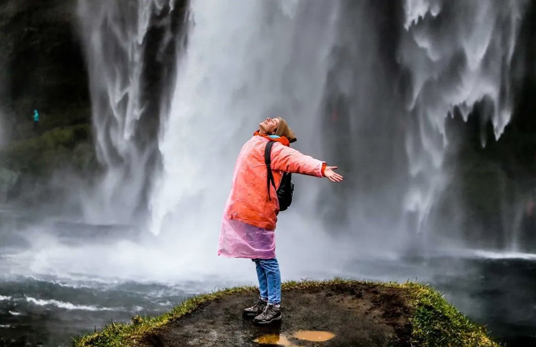 Traveller with open arms before a waterfall